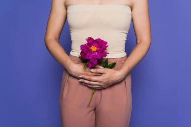 Mujer sujetando una flor en la zona de la pelvis