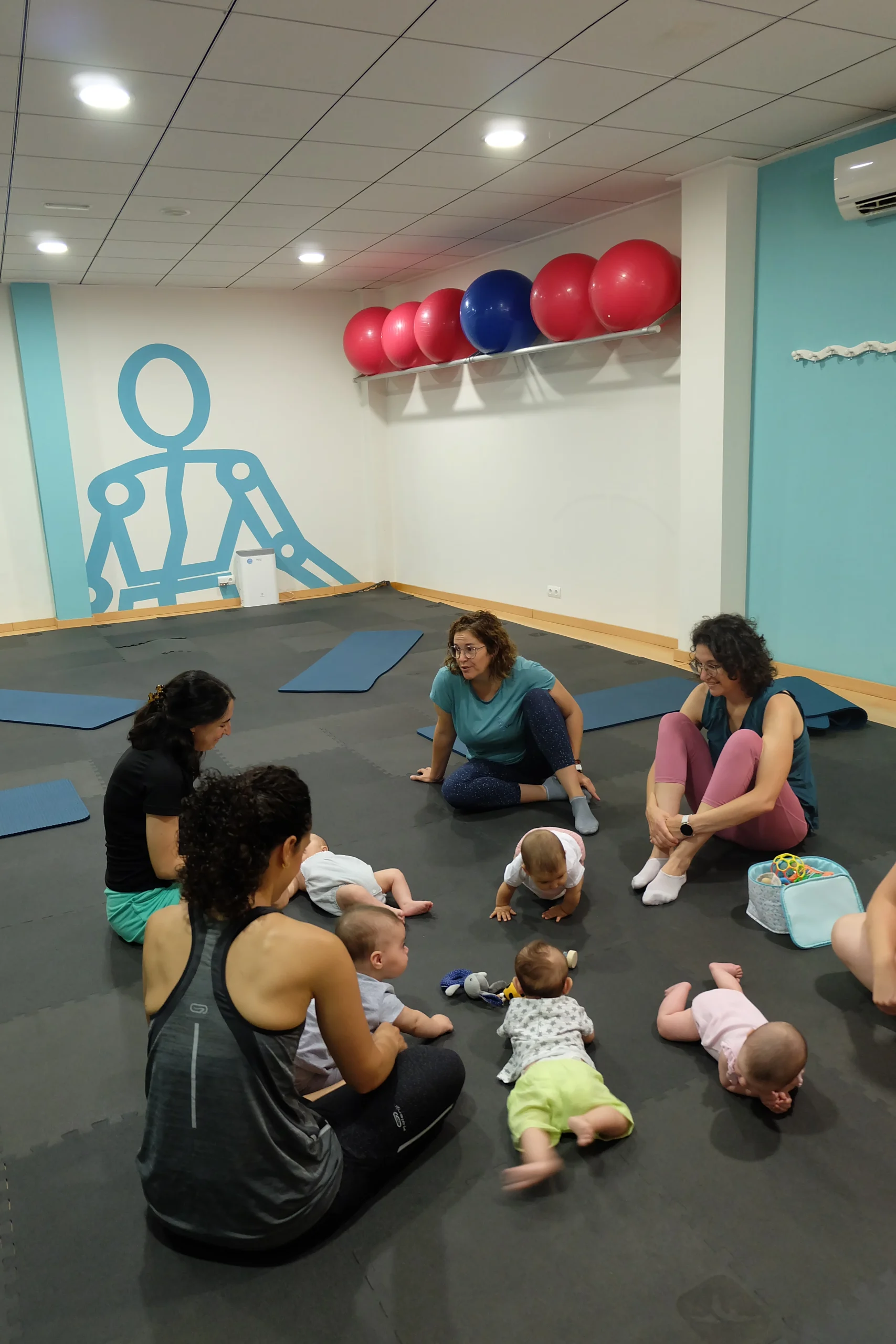 Mamás con sus bebés conversando sentadas en la colchoneta después de una clase de Recuperacion Postparto en la sala de pilates.